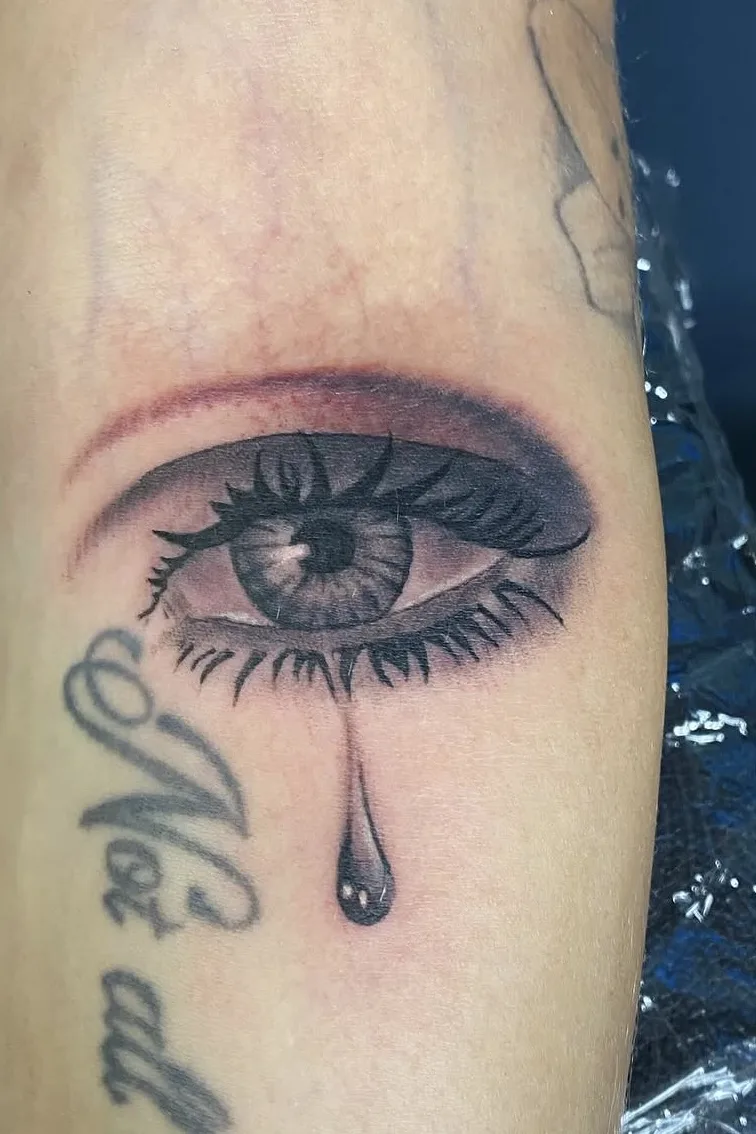 Realistic black and gray eye with teardrop and script lettering
