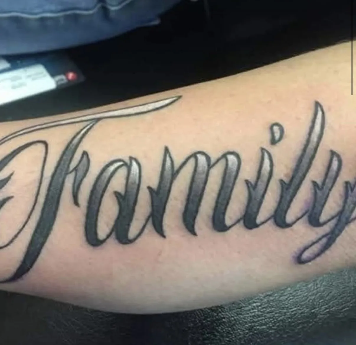 Script lettering tattoo reading Family on forearm